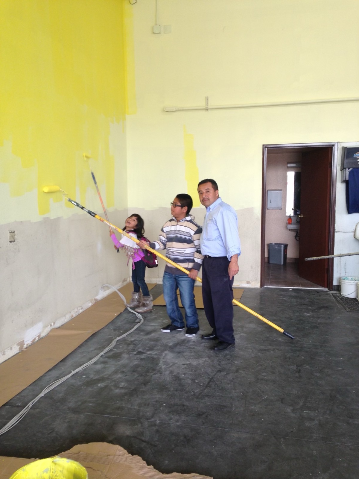 Servando Orozco in an Orozco's Auto Service shirt with his children, painting the walls of one of the family's shops