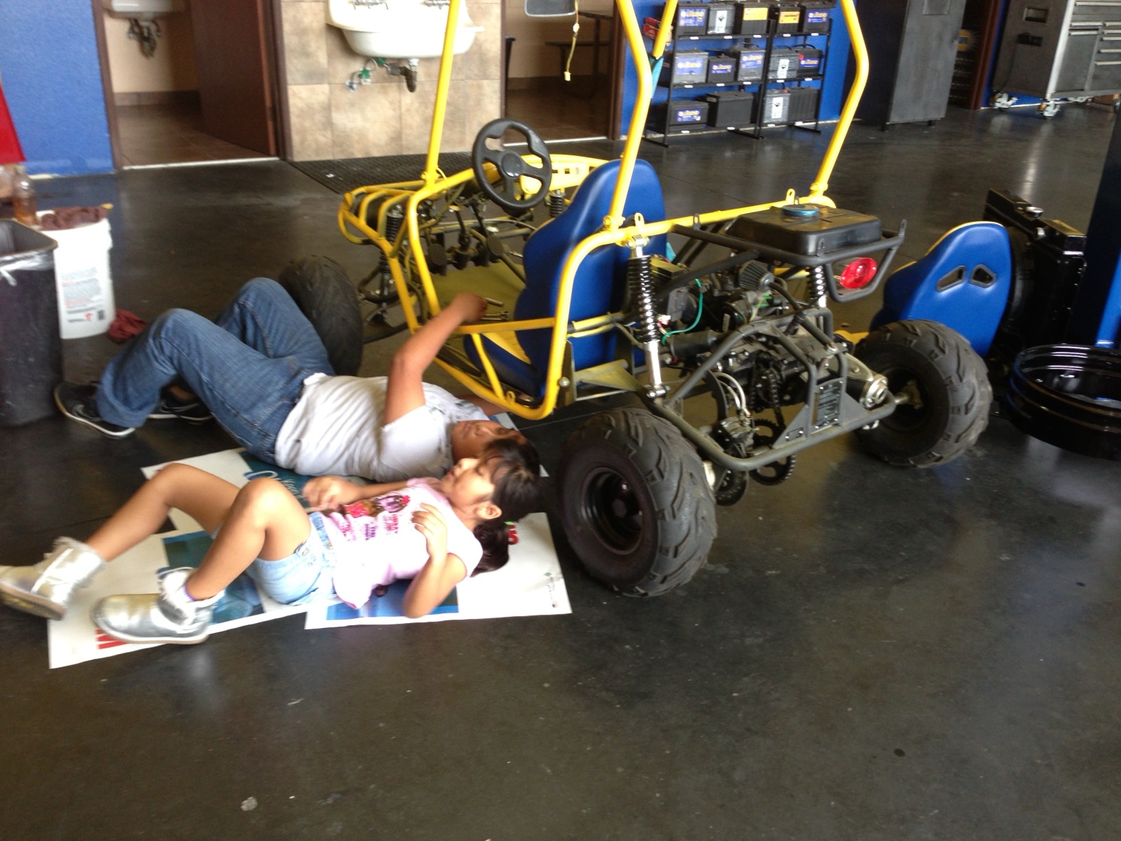 A young Andrew Orozco and his sister lying on the shop floor next to a go-kart