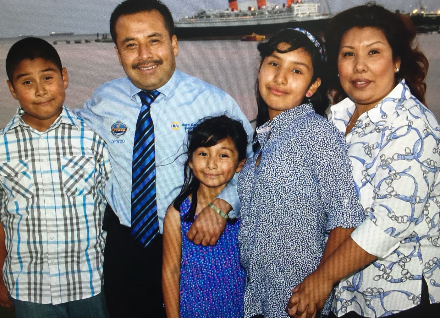 Servando Orozco in an Orozco's Auto Service shirt with his wife and three children, photographed in Long Beach with the Queen Mary behind them